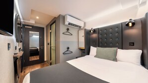 A modern hotel room with a large bed, a wall-mounted air conditioner, a bedside table, and a hanging light fixture. - Point A London Waterloo (London)