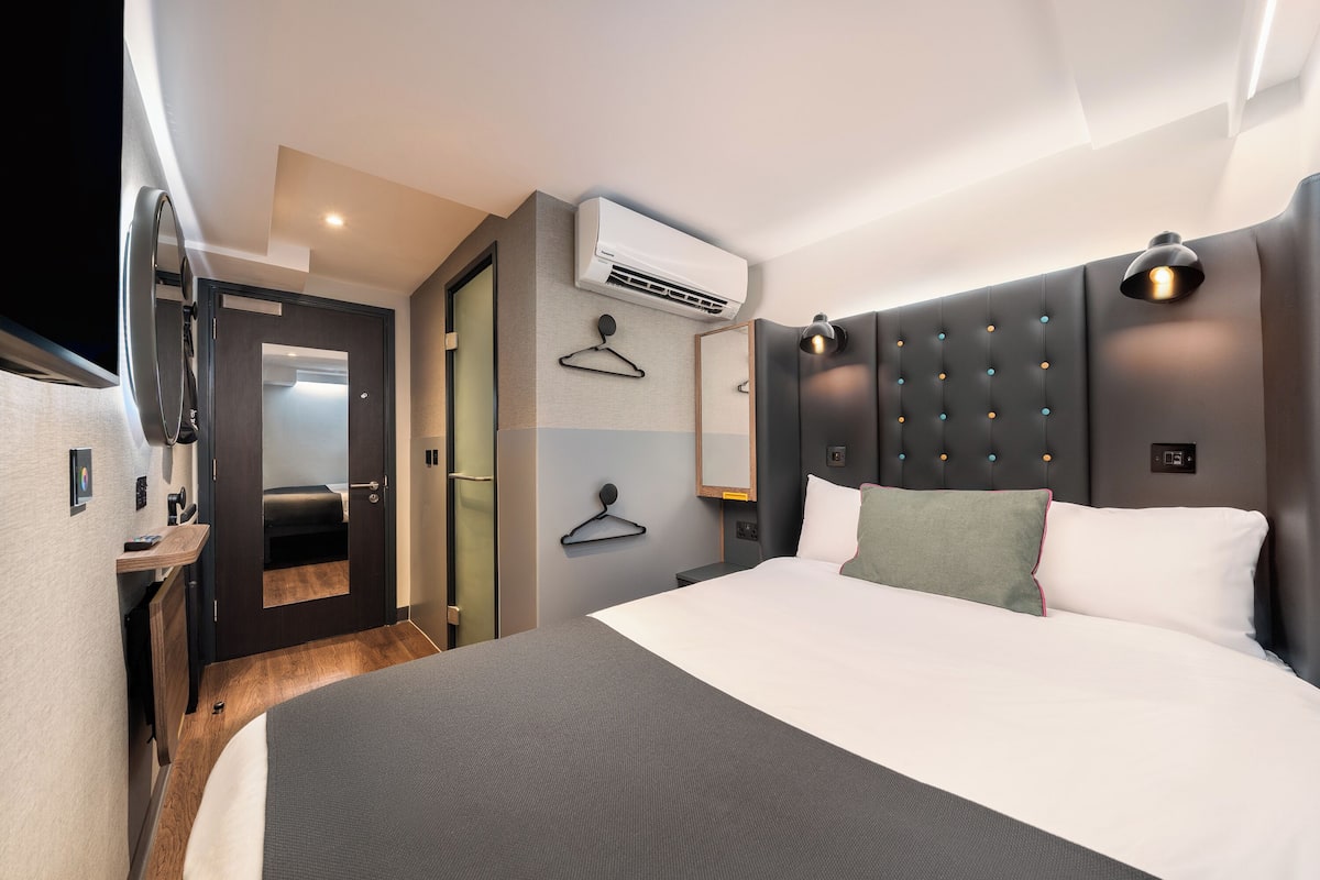 Ein modernes Hotelzimmer mit einem großen Bett, einer Klimaanlage, einem Spiegel und einer Nachttischlampe.