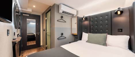 A modern hotel room with a large bed, a wall-mounted air conditioner, a bedside table, and a hanging light fixture.