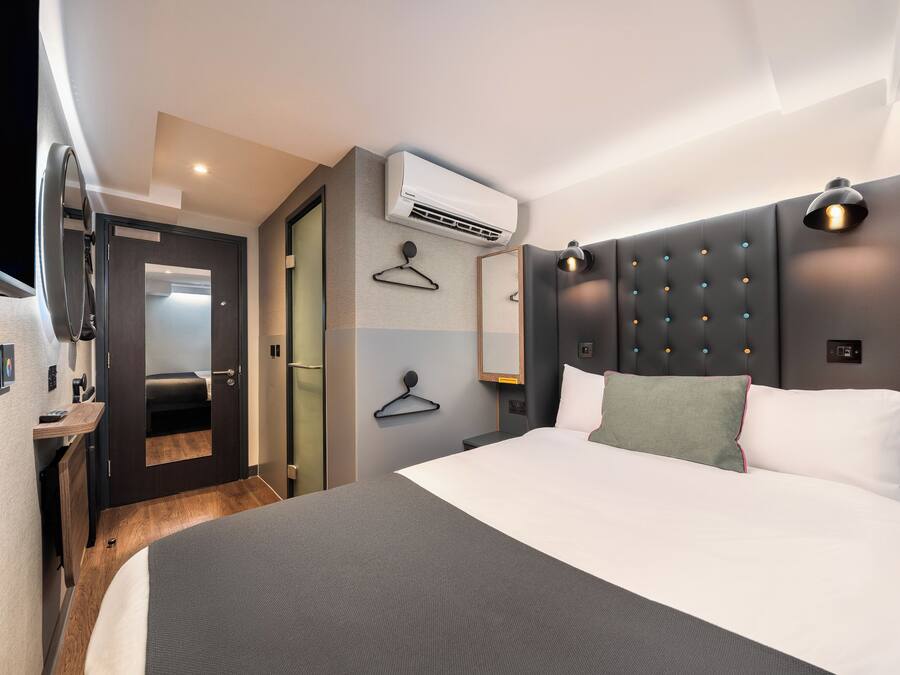 Una habitación de hotel moderna con una cama grande, aire acondicionado de pared, una mesita de noche y una lámpara colgante.