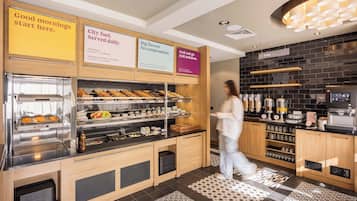 Un área de desayuno con estación de autoservicio, máquina de café y diversas opciones de comida.