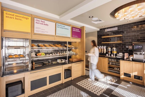 Ein Frühstücksbereich mit Selbstbedienungsstation, einer Kaffeemaschine und einer Auswahl an Speisen.