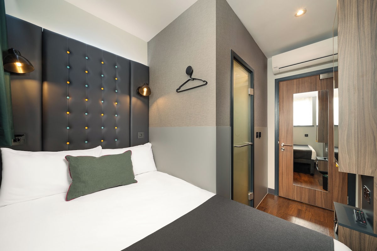 Ein modernes Hotelzimmer mit einem großen Bett, einer Pendelleuchte und einem Spiegel.