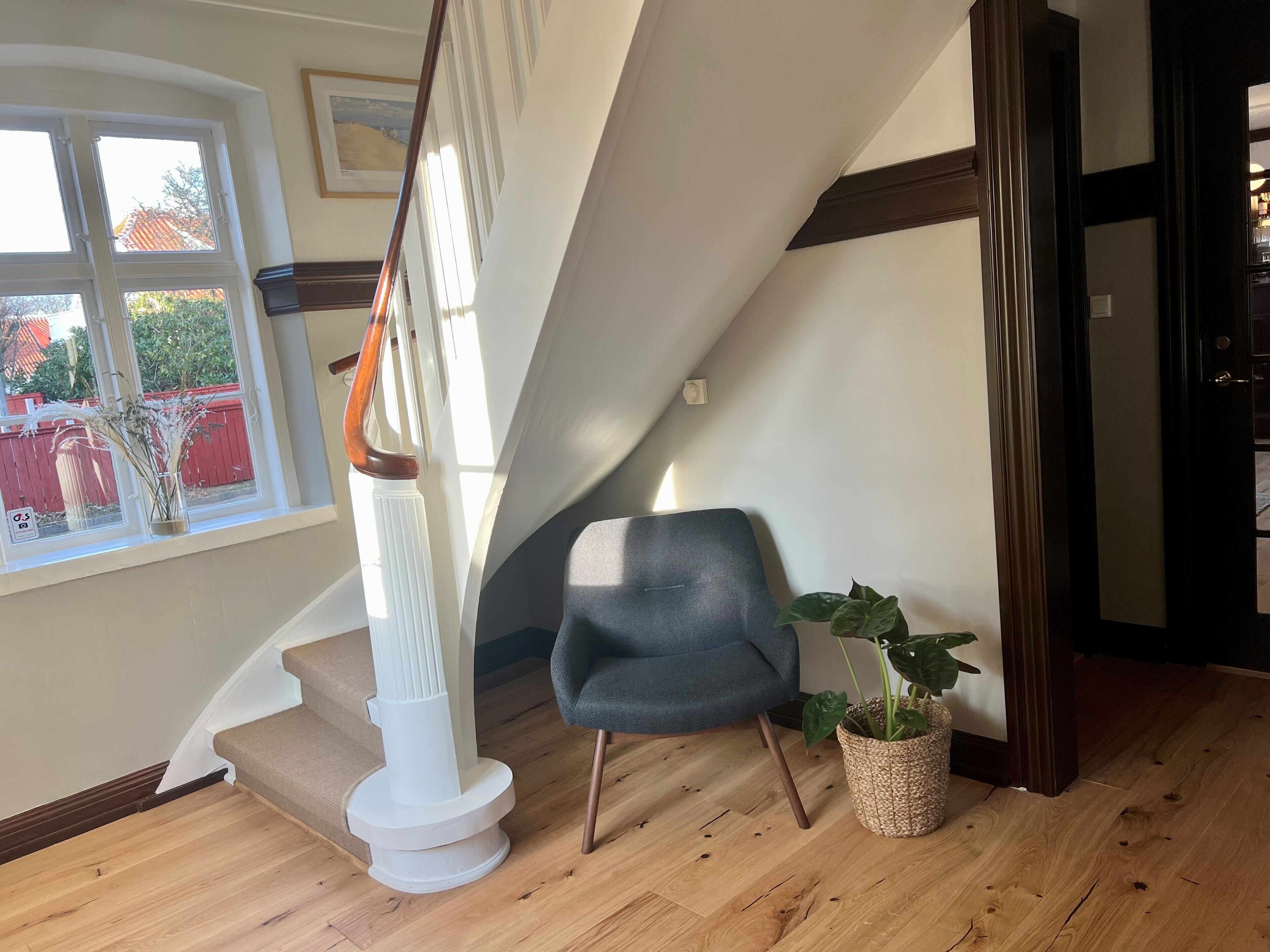 A staircase with a white column and wooden handrail, a blue chair, and a potted plant.
