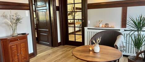 A room with a wooden floor, a round table with a vase and candle, a cabinet, and a door leading to another room.
