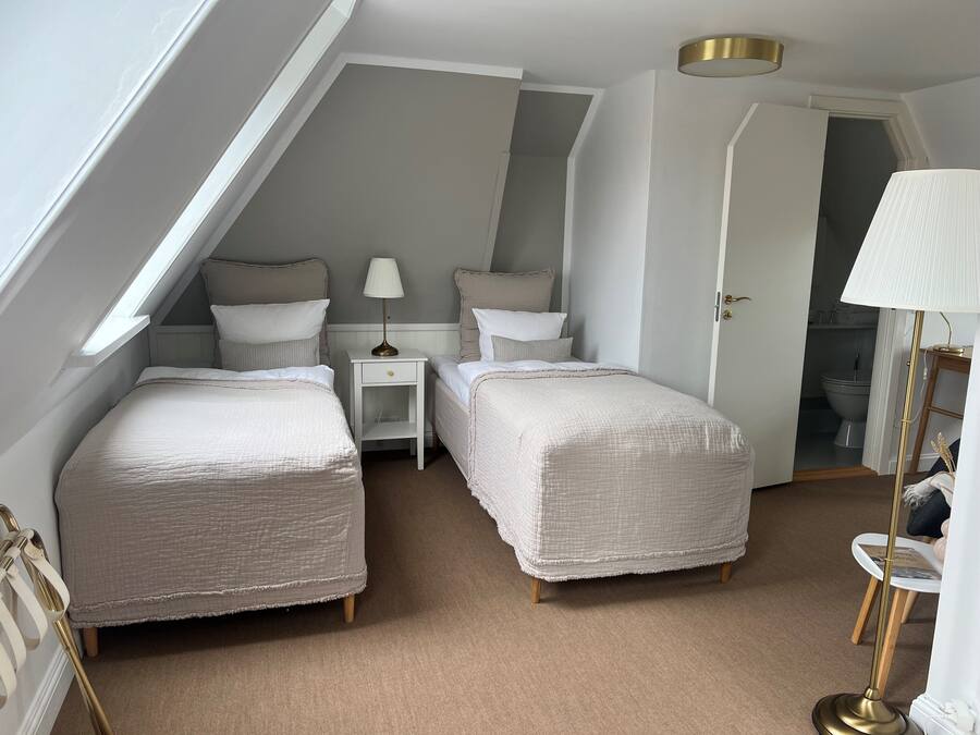 A bedroom with two beds, a nightstand, a lamp, and a door leading to a bathroom.