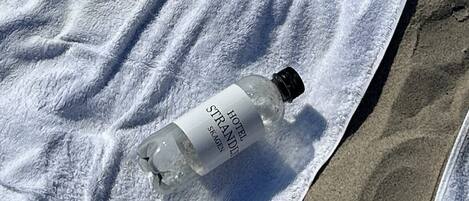 Une serviette blanche sur le sable, à côté d’une bouteille portant les inscriptions « HÔTEL STRAND » et « SKAGEN ».
