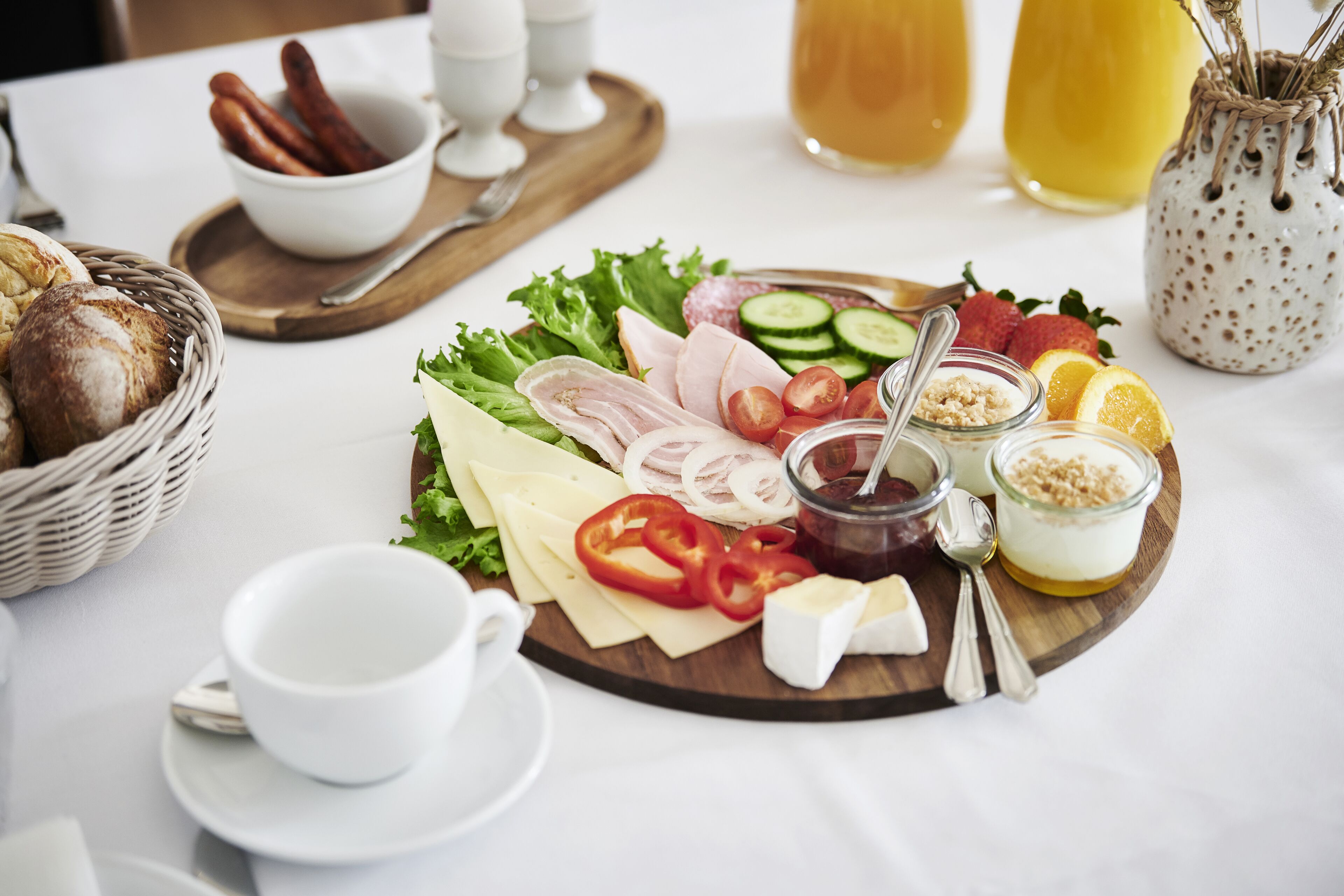 Een ontbijt met diverse soorten kaas, vleeswaren, groenten en sauzen, gepresenteerd op een houten plank.