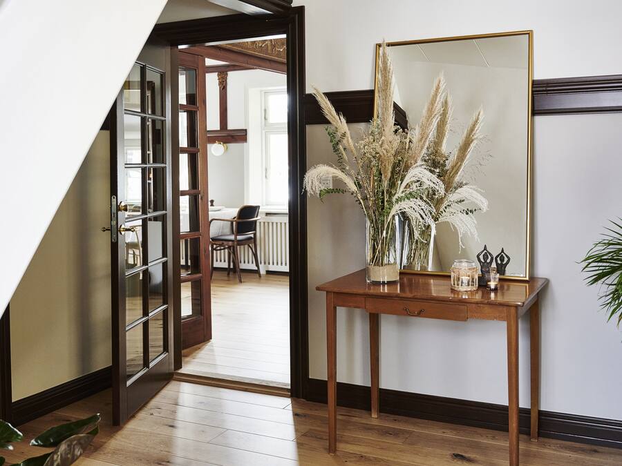 A wooden console table with a mirror, a vase with pampas grass, and a small plant.