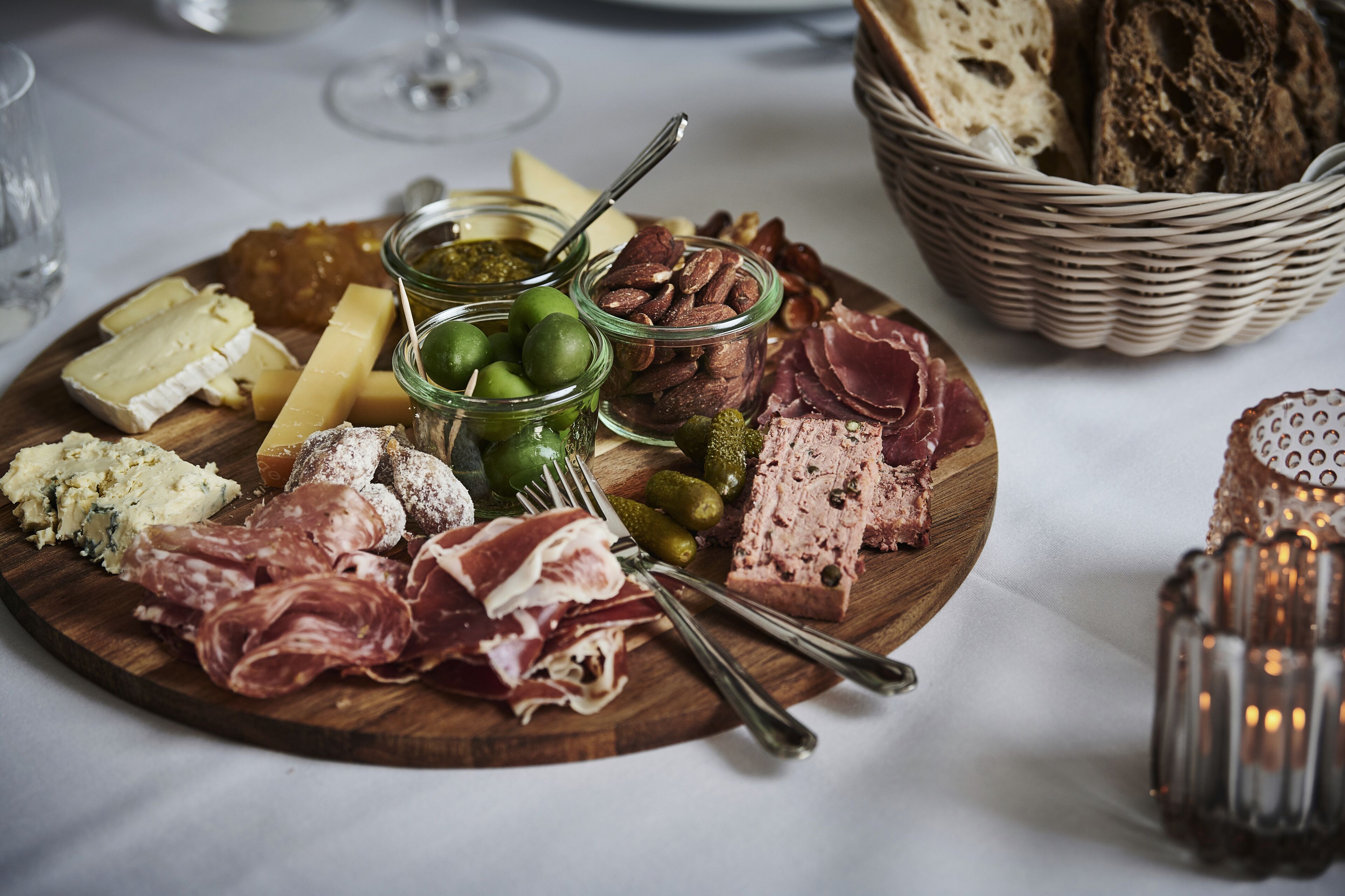 Uma tábua de madeira com diversos queijos, carnes e picles.