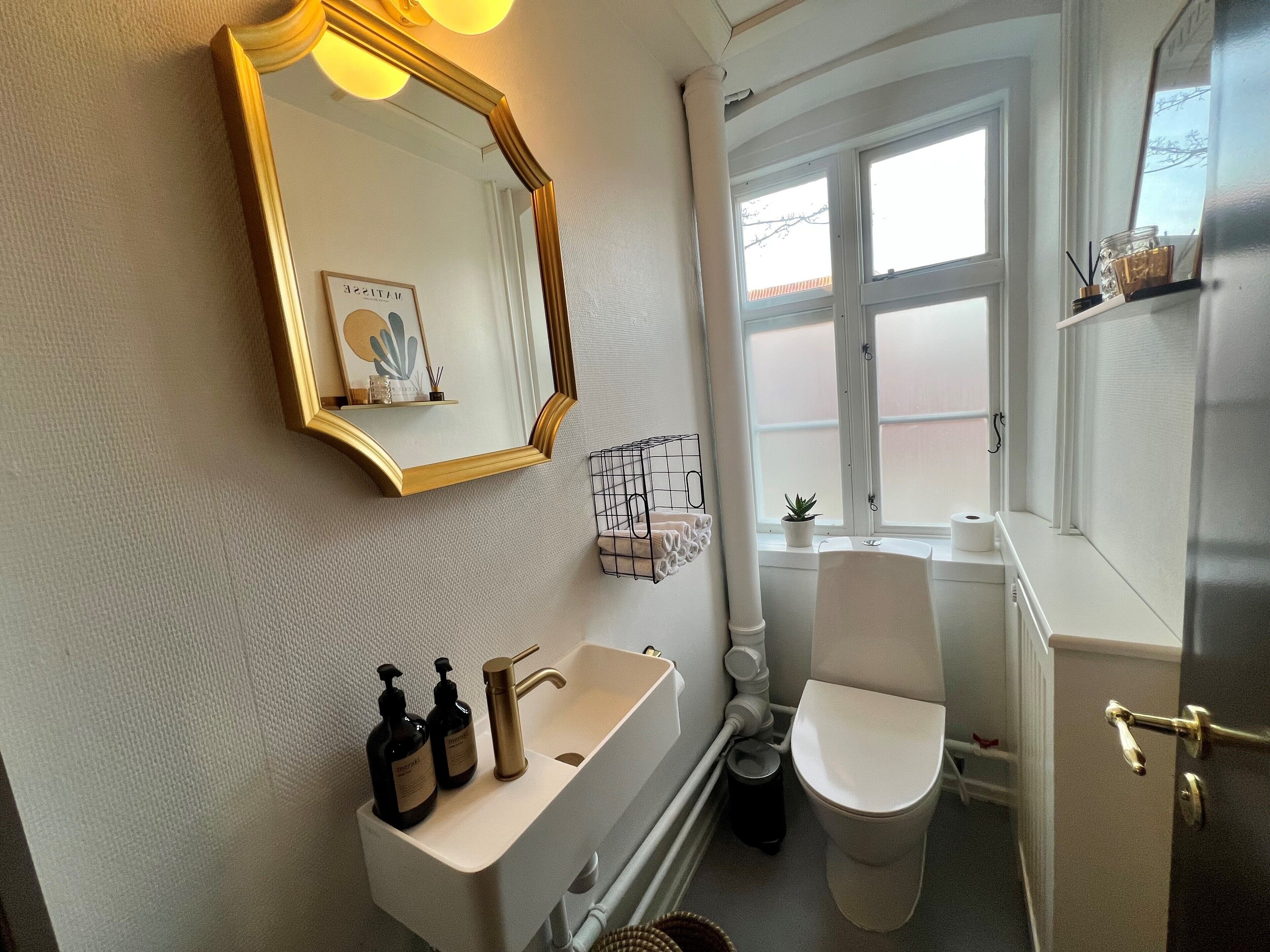 Un baño con un lavamanos blanco, un espejo con marco dorado, un inodoro y una ventana con vistas al exterior.