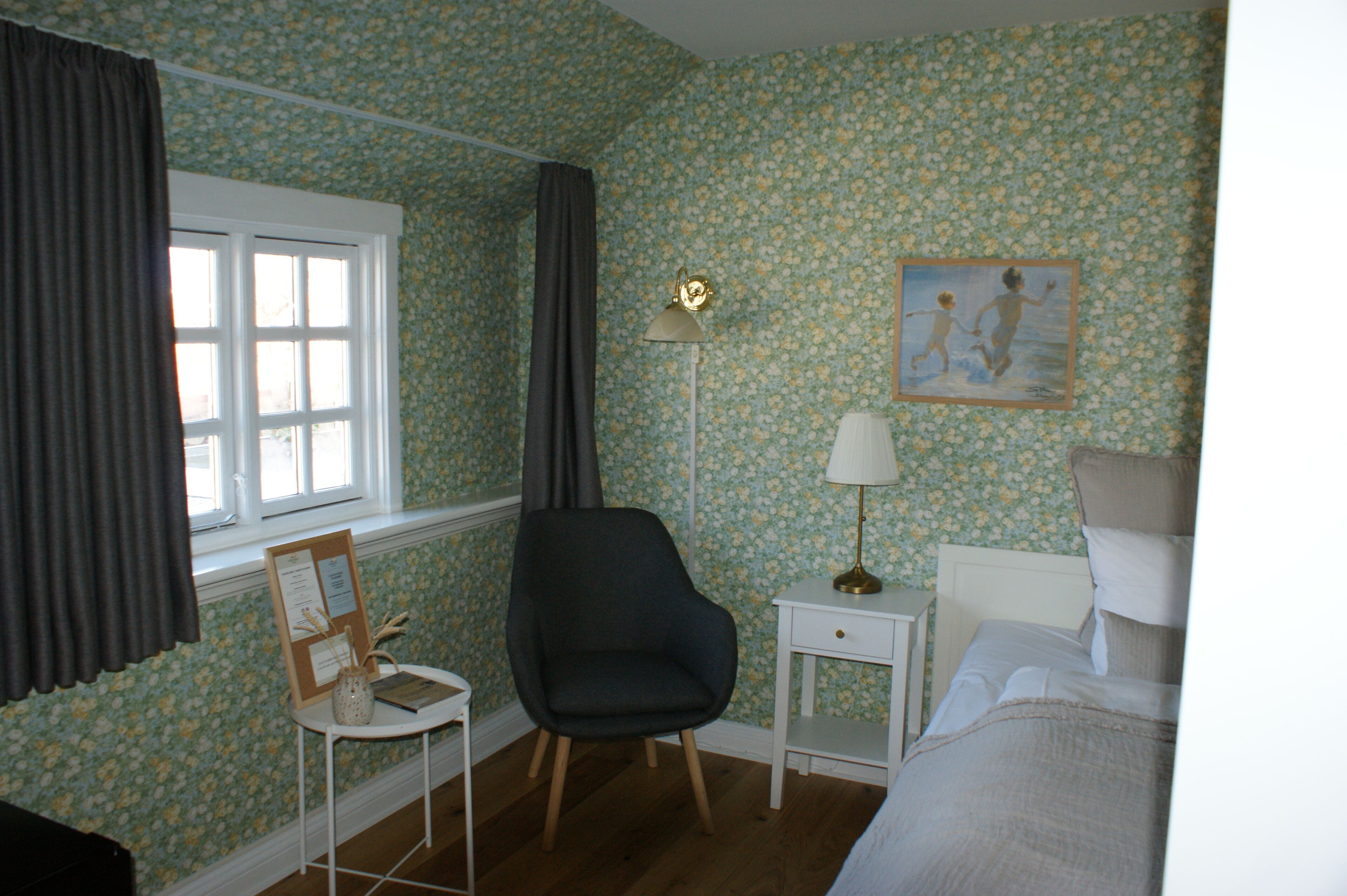 Et soveværelse med blomstret tapet, en stol, et natbord med lampe og en seng.