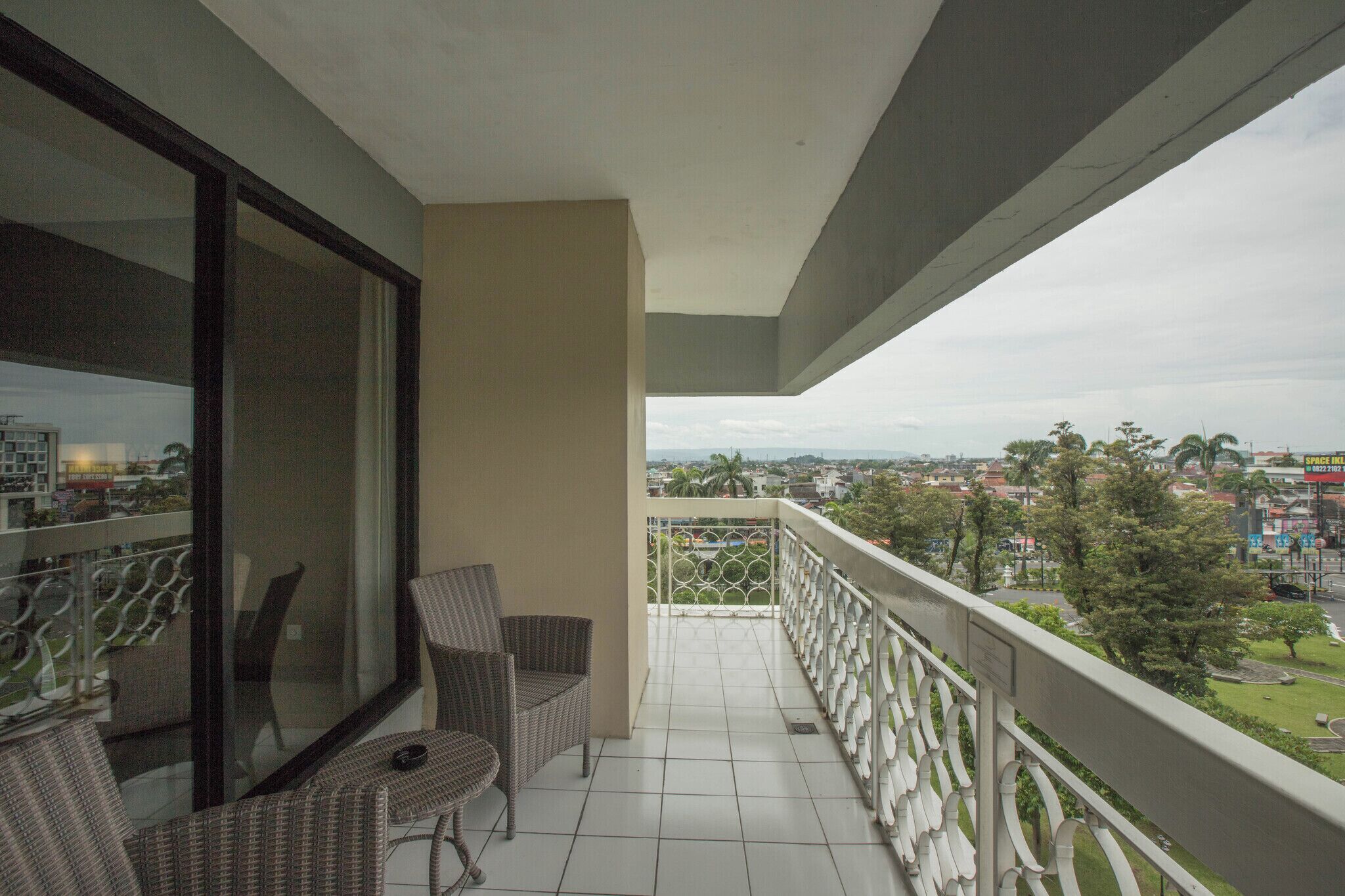 Un balcón con dos sillones de mimbre, un ventanal de vidrio y vista a un paisaje urbano.