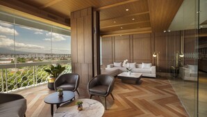 A modern living room with a large sofa, two armchairs, and a coffee table. There is a balcony with a view of the city. - Royal Ambarrukmo Yogyakarta (Depok)