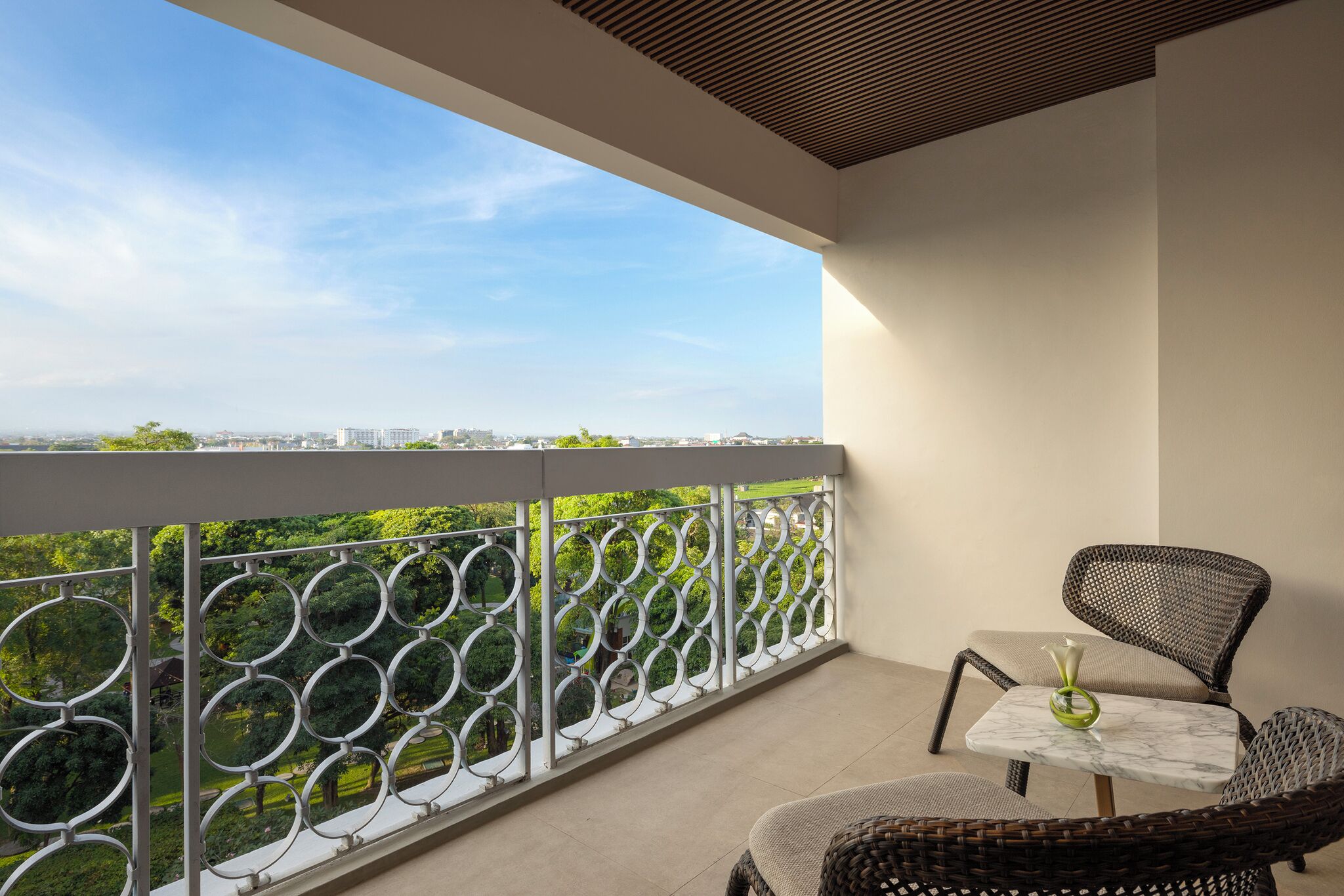 Ein Balkon mit Blick auf eine Stadtlandschaft, ein Korbstuhl und ein kleiner Tisch mit einer Vase.