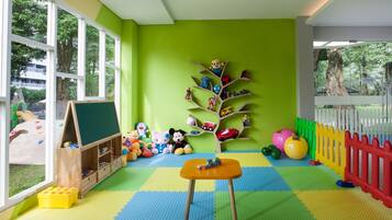 A brightly colored playroom with a large window, a wooden play table, and a toy tree shelf.