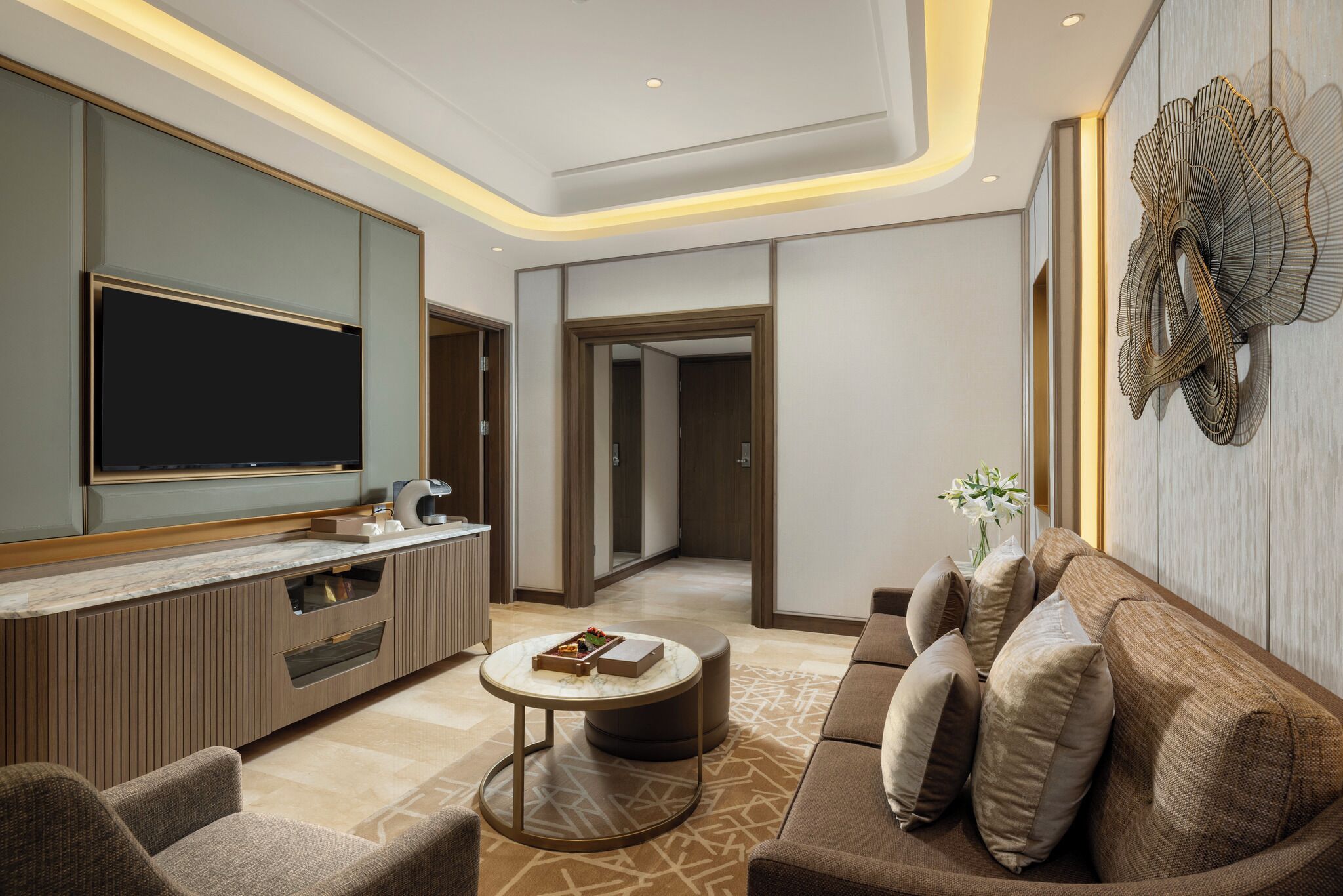 A modern living room with a large flat-screen TV, a sofa, a coffee table, and a decorative wall piece.