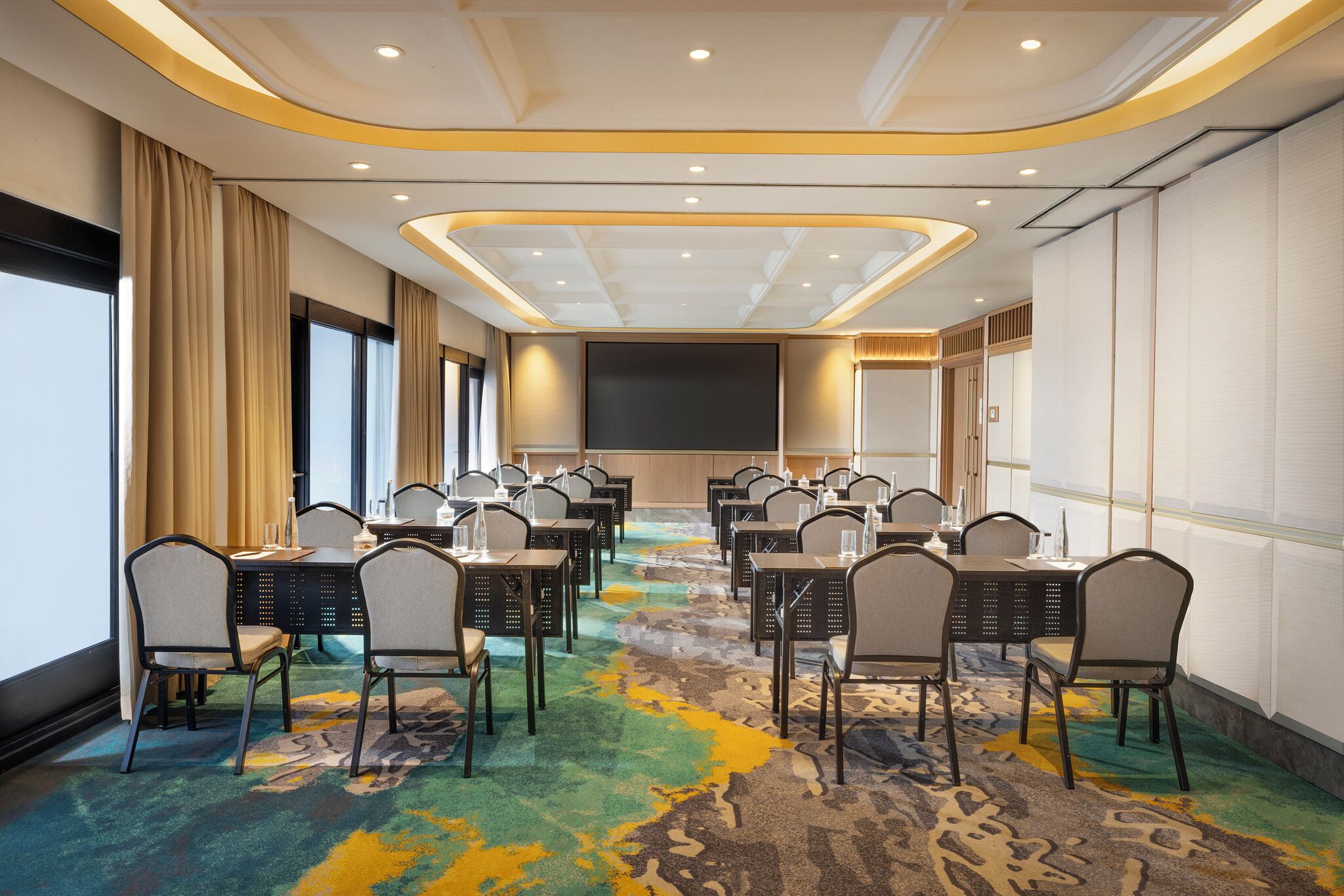 A conference room with multiple tables and chairs, a large screen, and a colorful carpet.