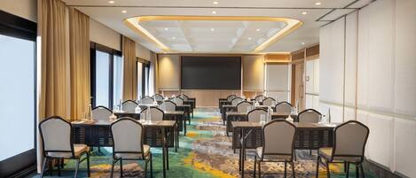A conference room with multiple tables and chairs, a large screen, and a colorful carpet.