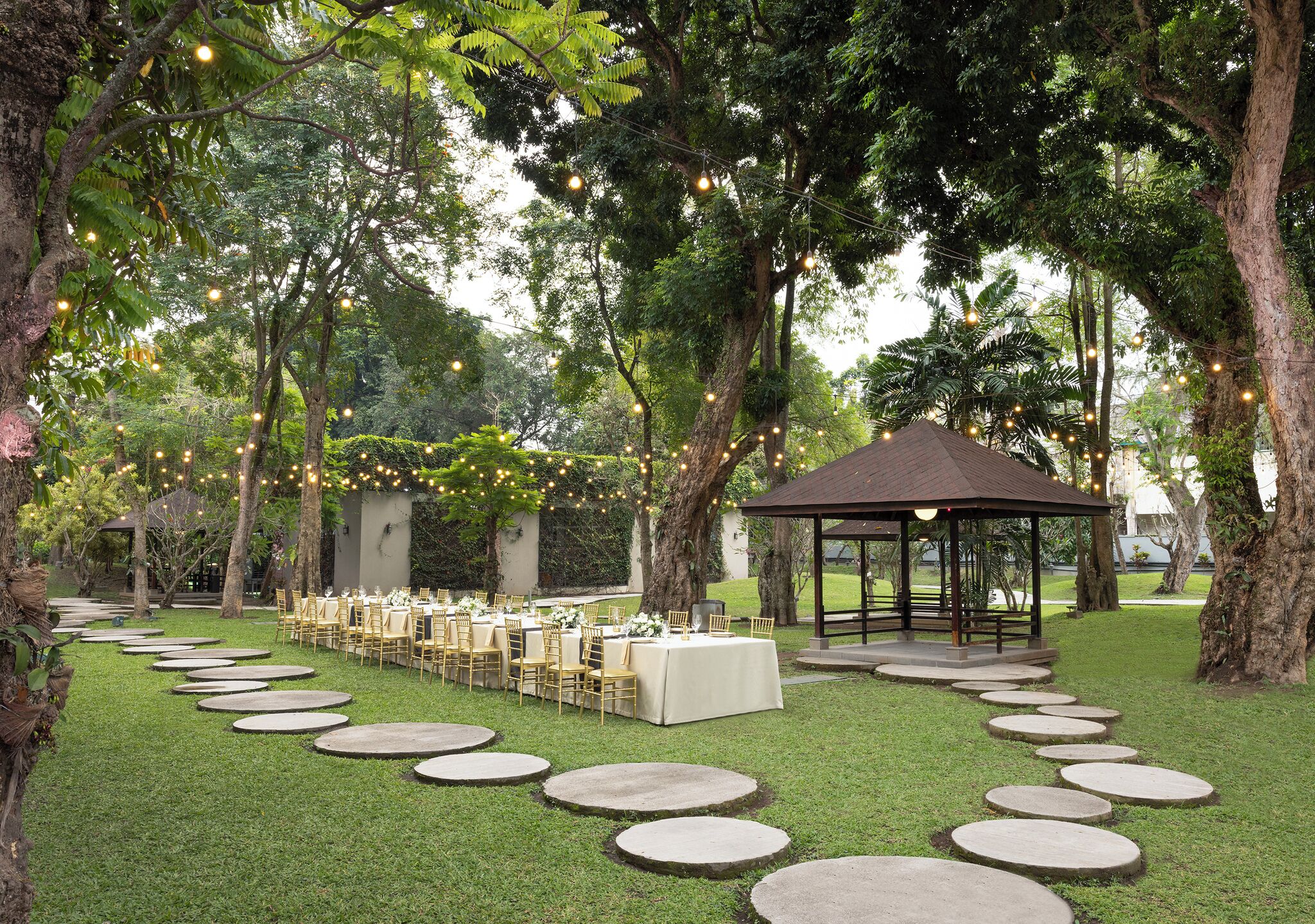 Location per matrimonio all'aperto con un lungo tavolo apparecchiato per gli invitati, circondato da alberi e un gazebo.