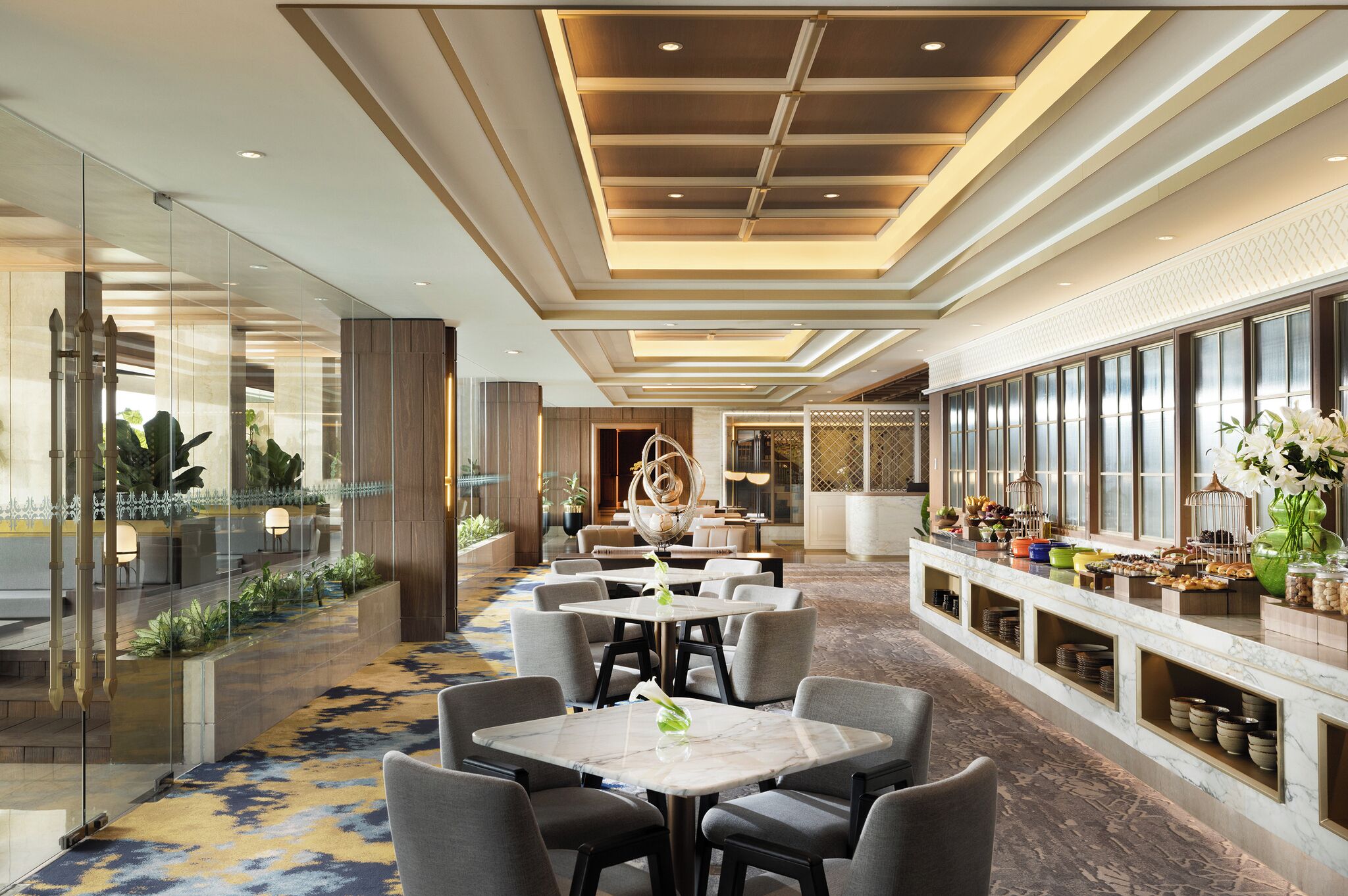 A hotel lobby with a long reception desk, seating area with tables, and a buffet with various food items.