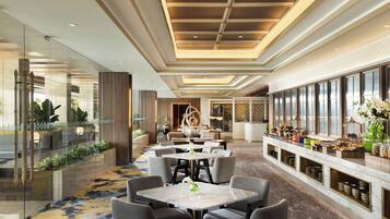 A hotel lobby with a long reception desk, seating area with tables, and a buffet with various food items.