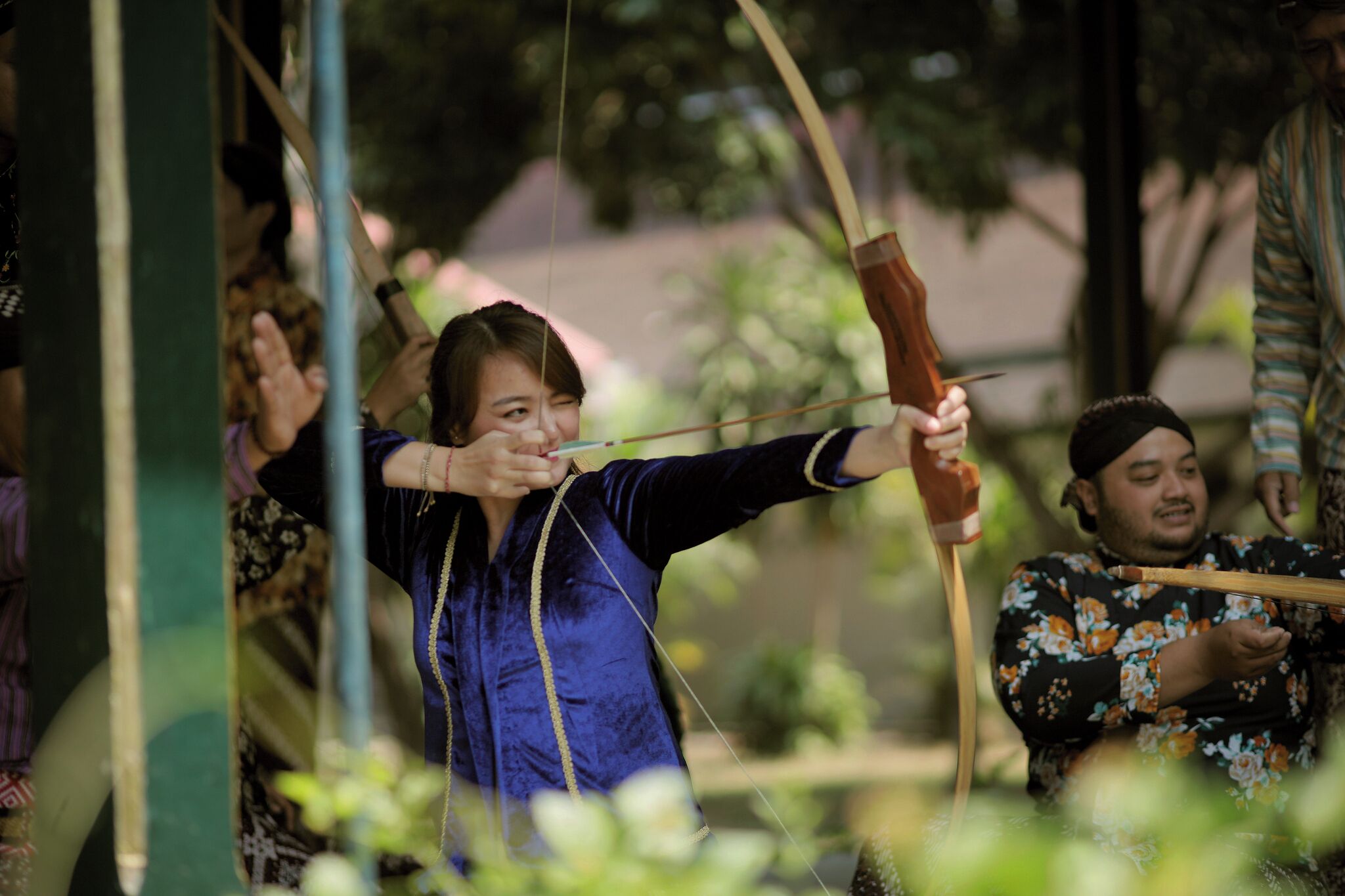 A person aiming a bow with a target in the background.