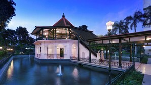 A building with a red roof and a glass enclosure, surrounded by a water feature and a walkway.