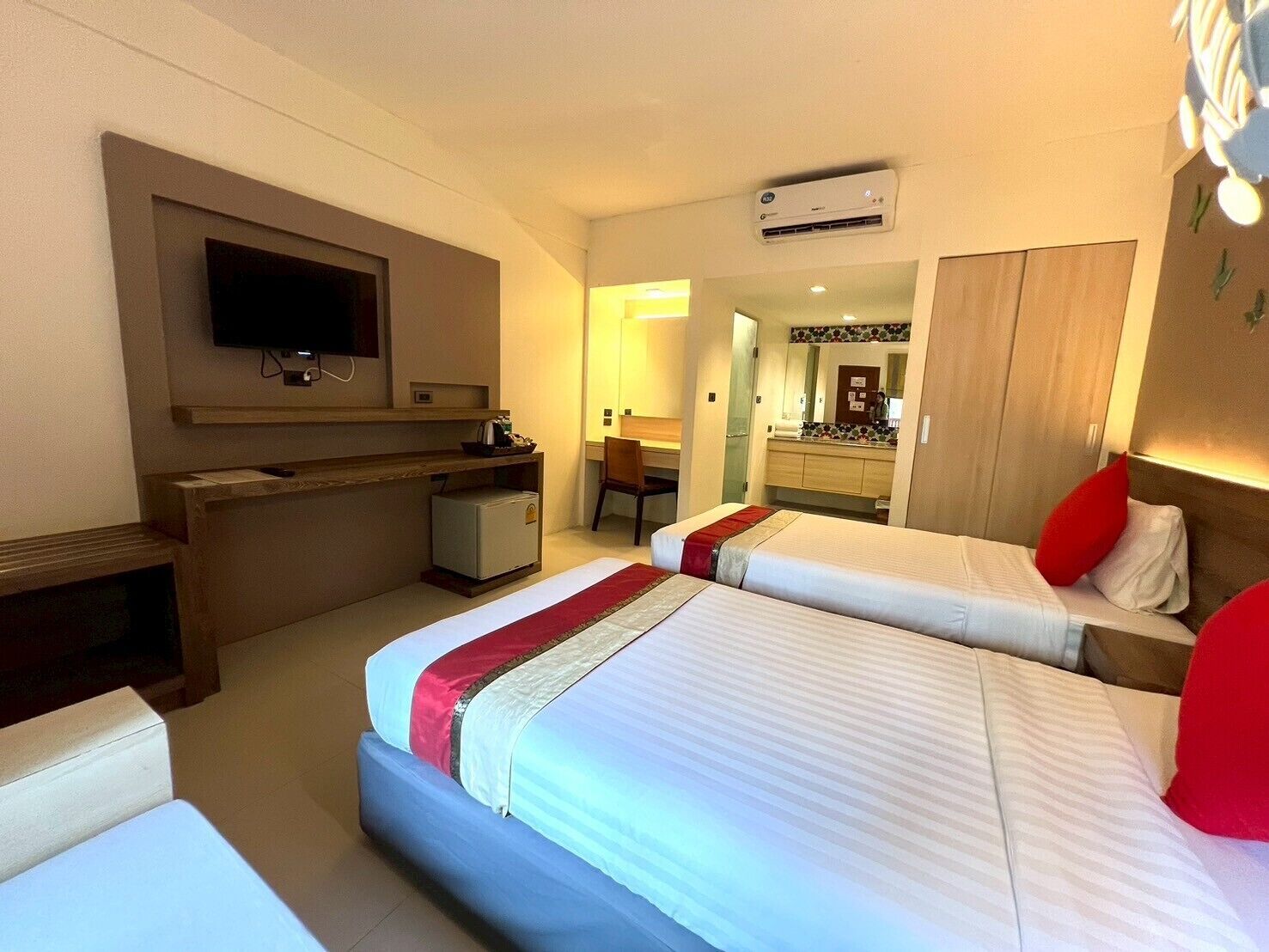 A hotel room with two beds, a desk, a television, and an air conditioning unit.