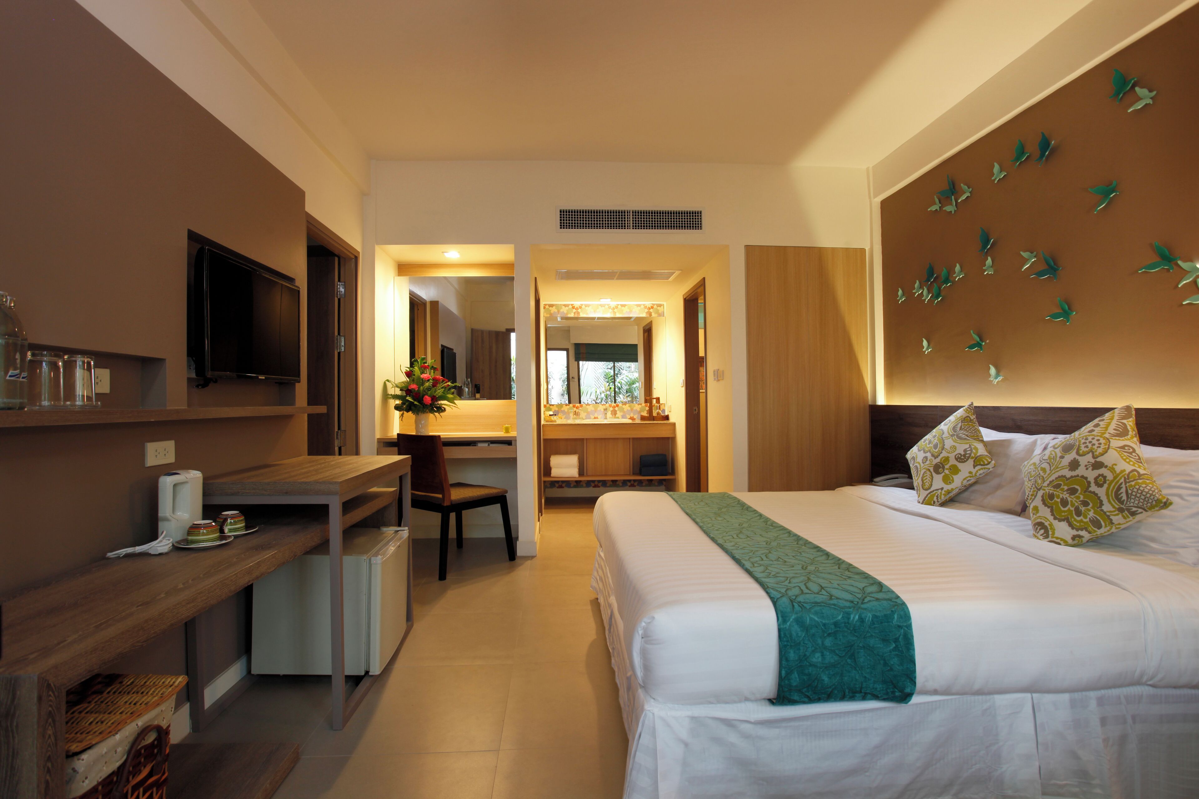 A hotel room with a bed, a desk, a chair, a TV, and a bathroom visible through an open door.