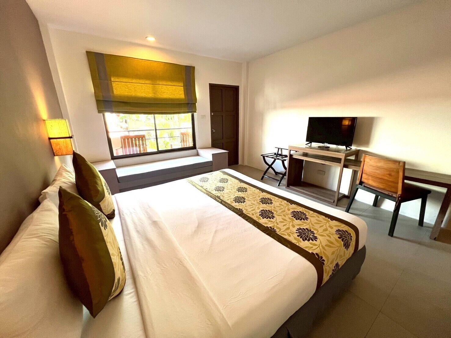 A hotel room with a large bed, a desk with a TV, a window with a view, and a door.