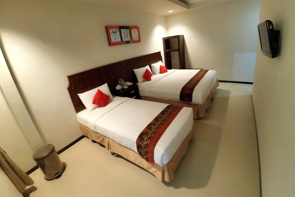 A hotel room with two beds, a wooden headboard, a small trash bin, and a television mounted on the wall.