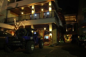 A building with a double balcony, a parked vehicle, and a statue.