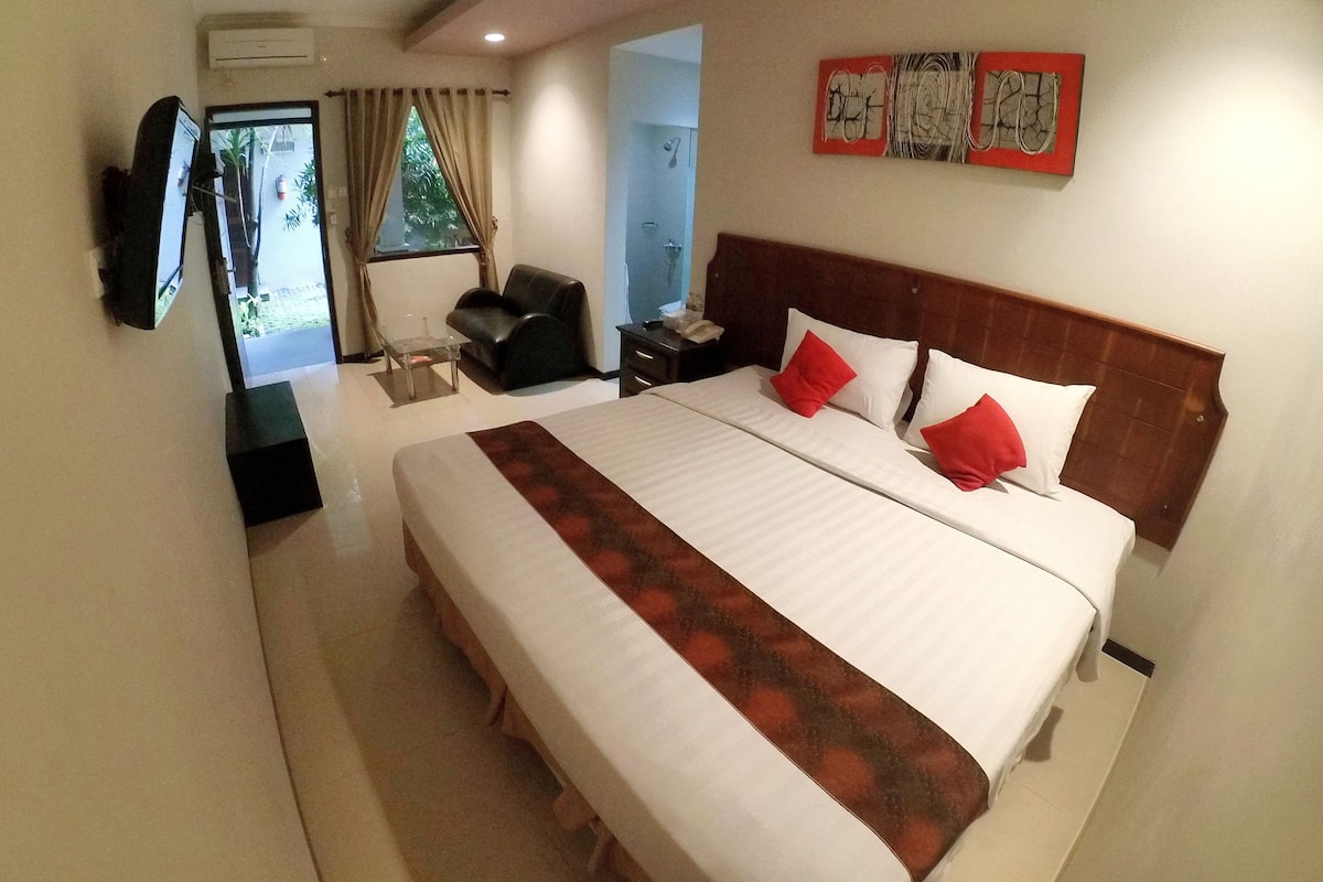 A hotel room with a large bed, a desk, a chair, and a TV mounted on the wall.
