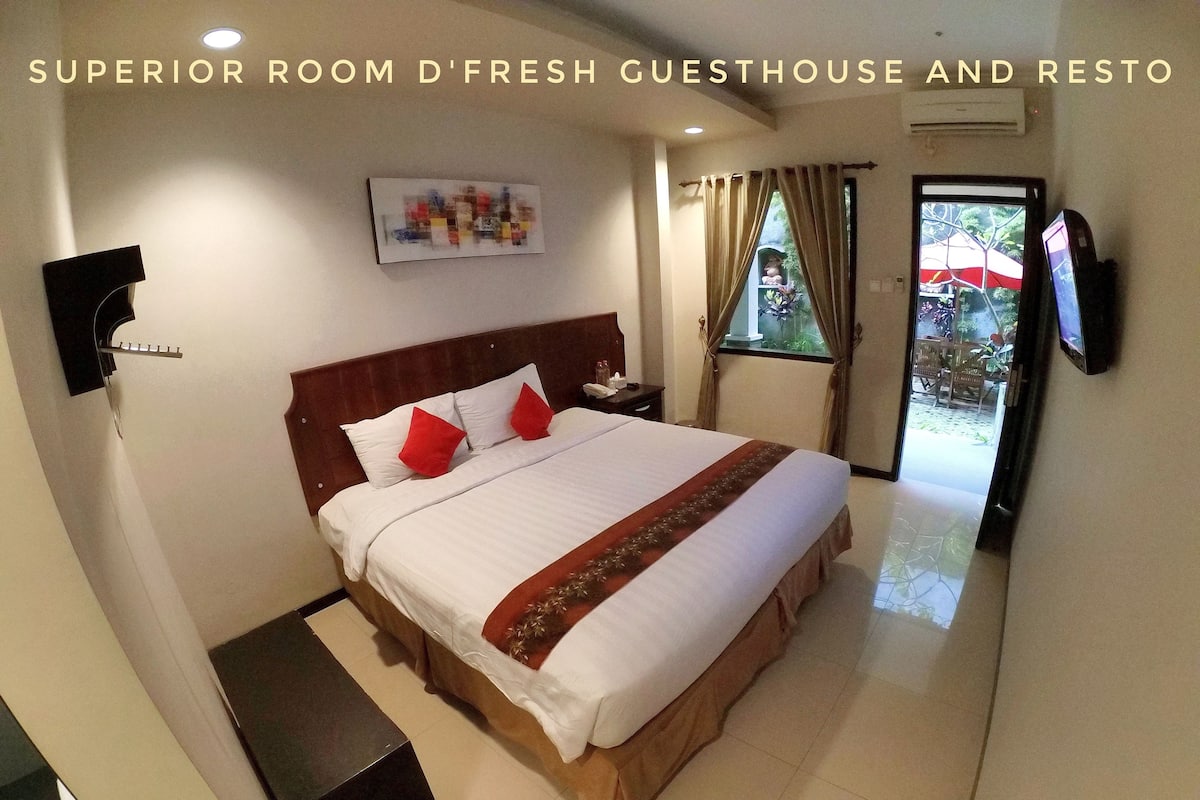 A hotel room with a bed, a TV, a window with curtains, and a wall-mounted air conditioner.