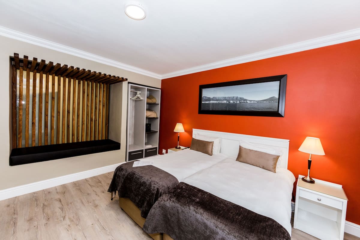 Un dormitorio con una cama, dos mesitas de noche con lámparas, un armario, una ventana con persianas y un cuadro en la pared.