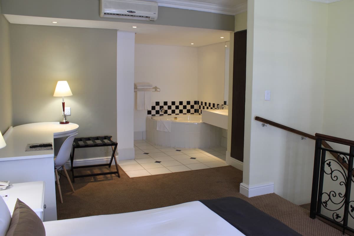 Habitación de hotel con cama, escritorio, silla, baño con bañera y pared a cuadros.
