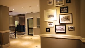 A hallway with framed pictures on the wall, a reception desk, and a staircase. - The New Tulbagh Hotel (Cape Town)