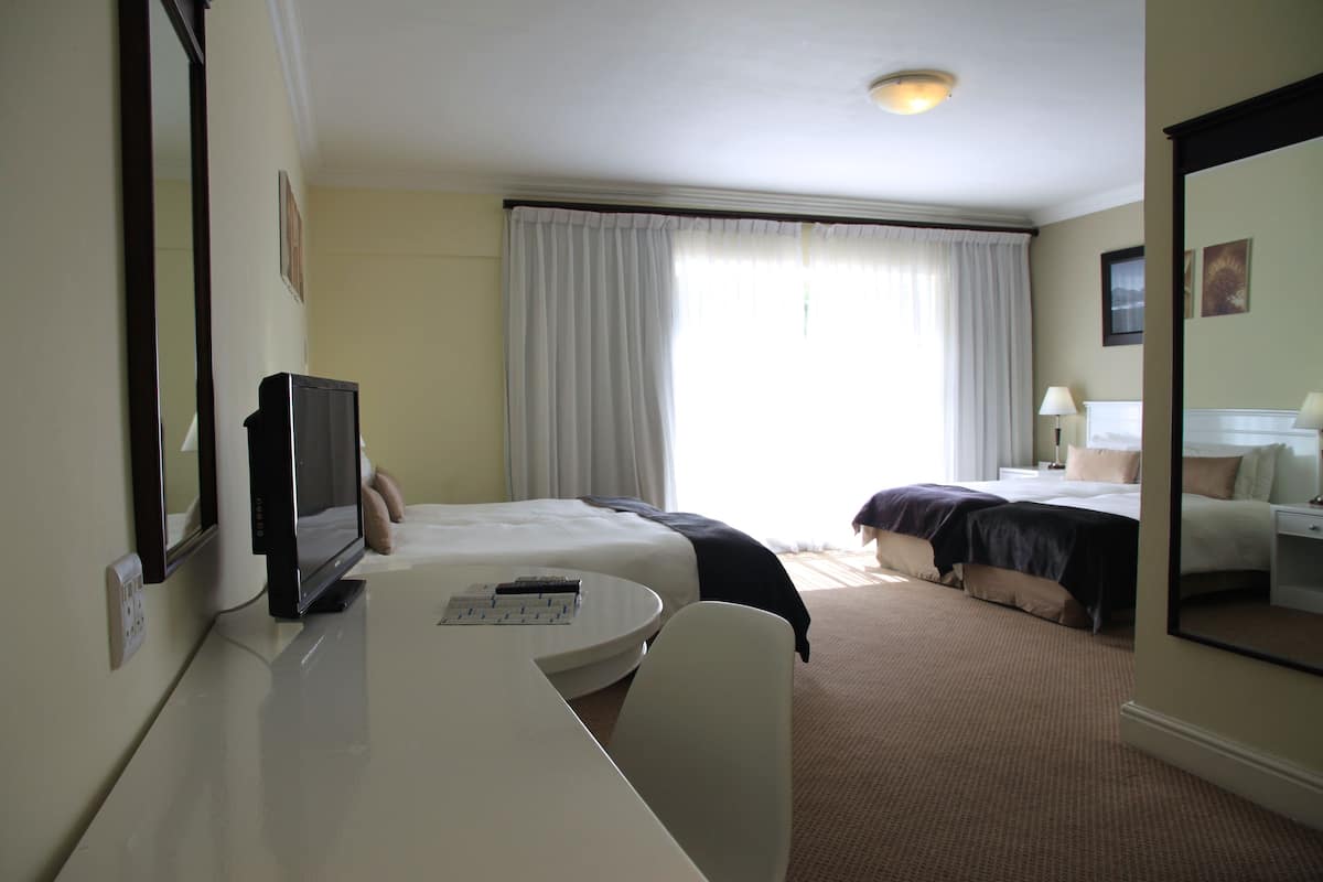 Una habitación de hotel con una cama, un escritorio con computadora, una silla y un espejo grande.