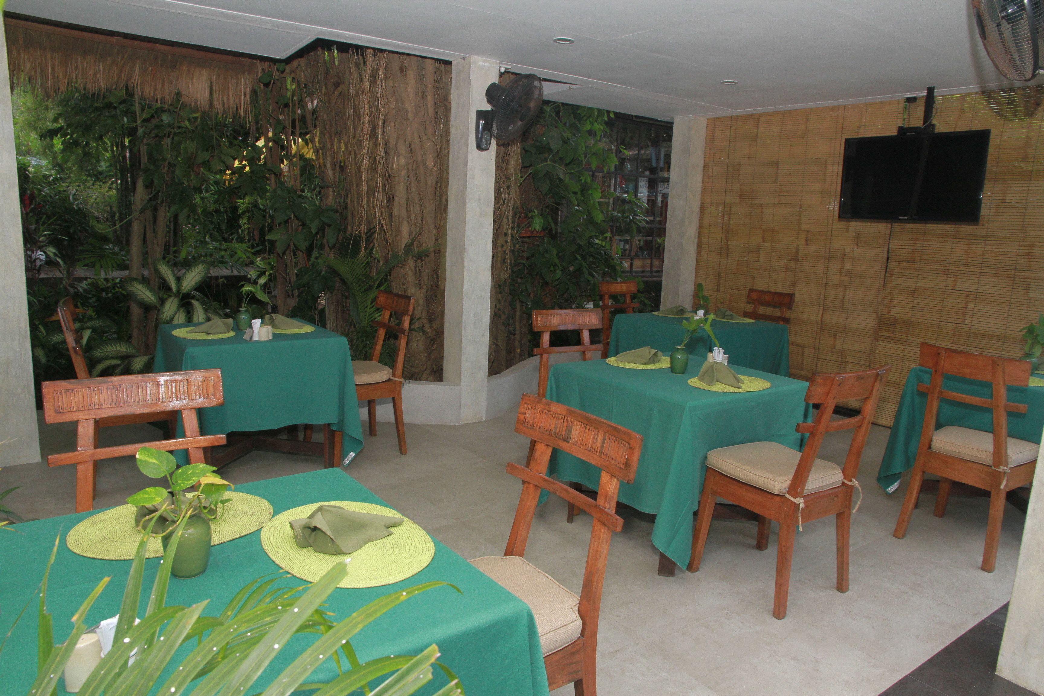 Un restaurante con mesas verdes y sillas de madera, rodeado de plantas.