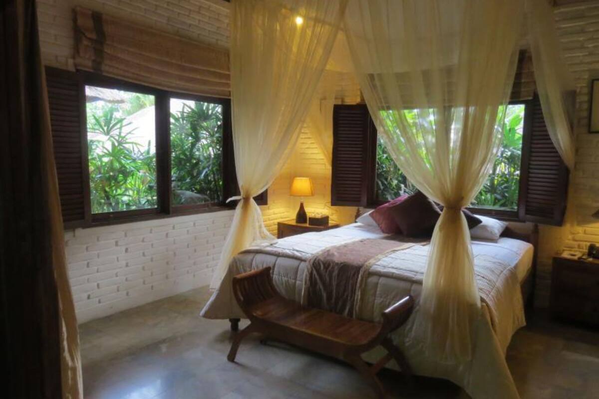 A bedroom with a bed, bedside tables, a bench, and a window with curtains.