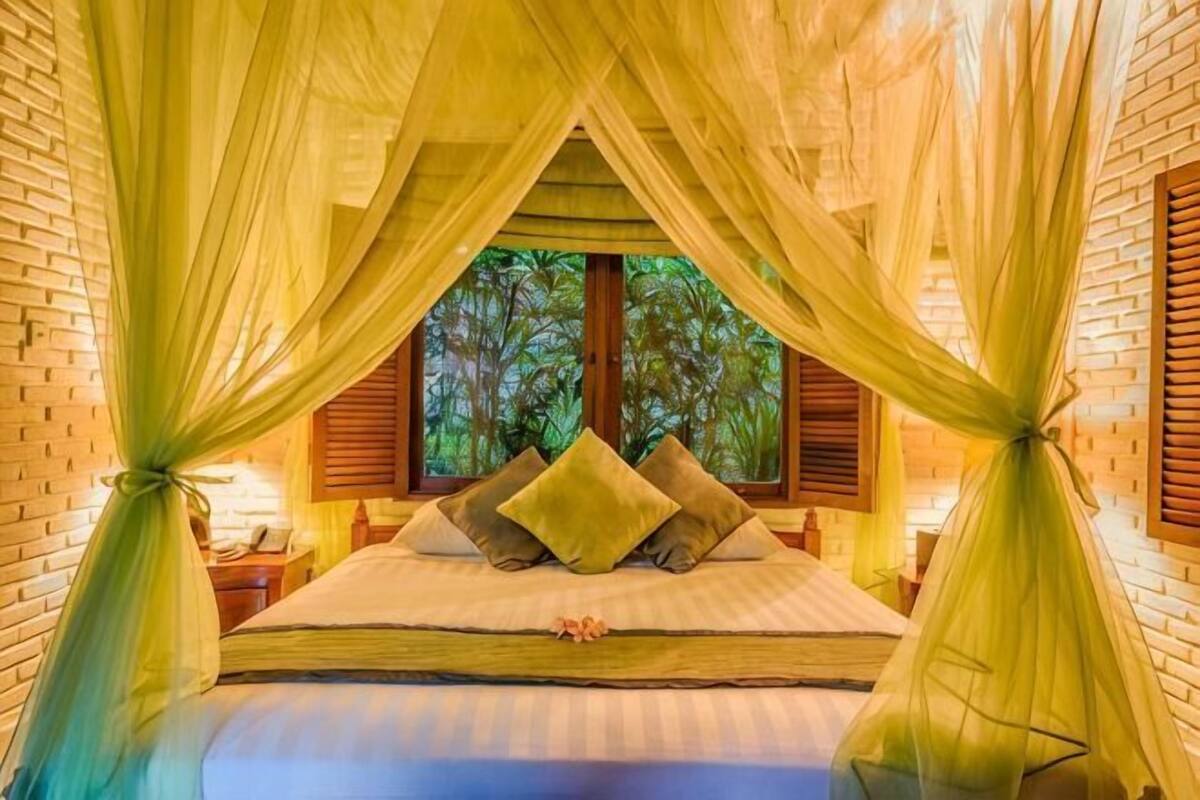 A bed with a canopy, pillows, and a window with a view of trees.