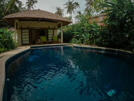 Una piscina con una estructura de techo de paja, rodeada de exuberante vegetación tropical.