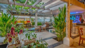 Un espacio interior con una pérgola de madera, plantas en macetas y arreglos de asientos.