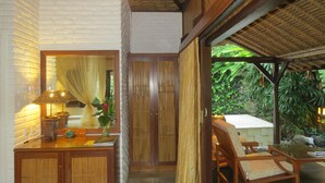 Una habitación con un escritorio de madera, una silla, una lámpara y vistas al exterior con vegetación.
