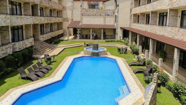 Un patio de hotel con piscina central, varios balcones y zonas de estar al aire libre.