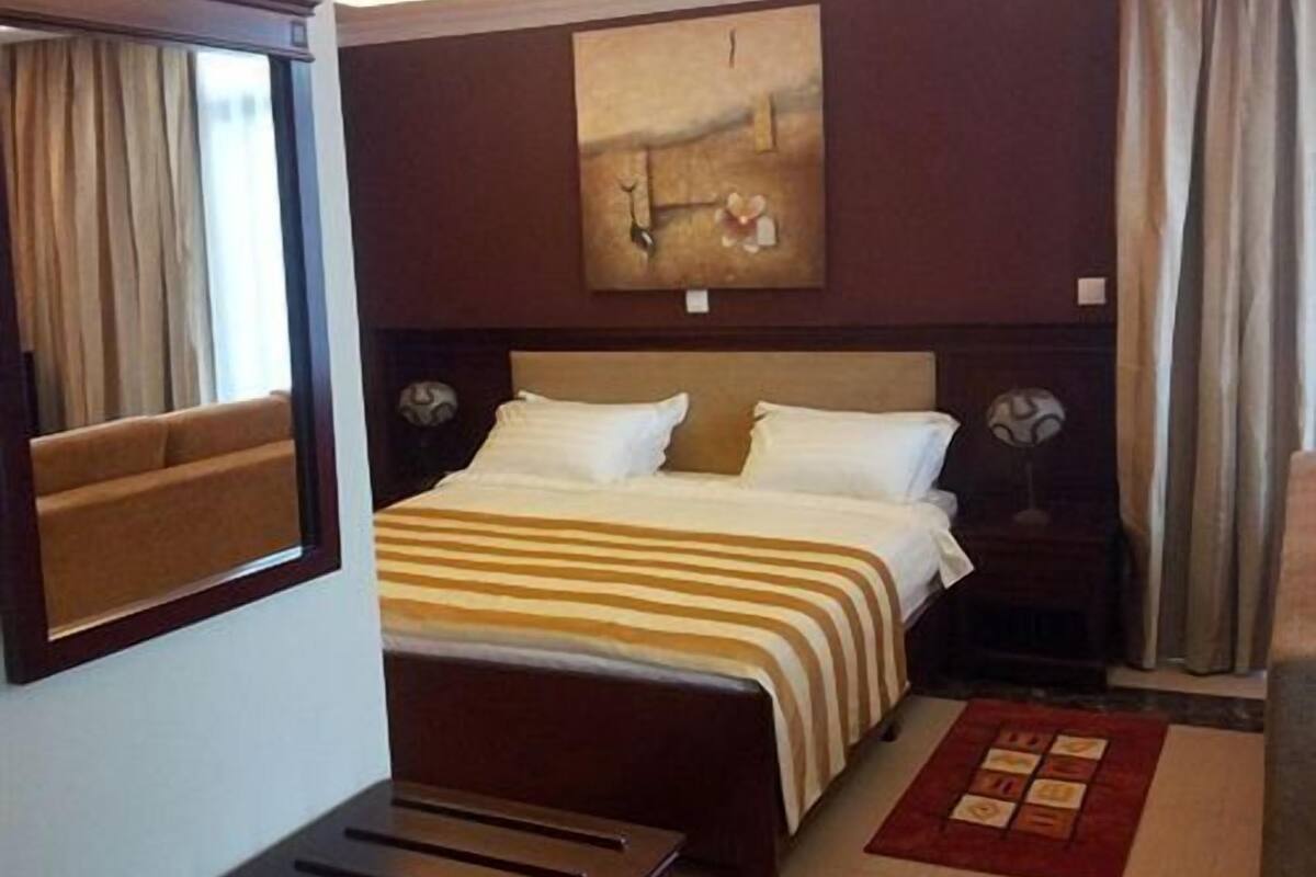 A hotel room with a bed, a nightstand, a bedside table, a mirror, and a painting on the wall.