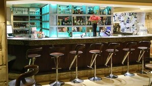 Zona de bar con varios taburetes y estanterías llenas de botellas.