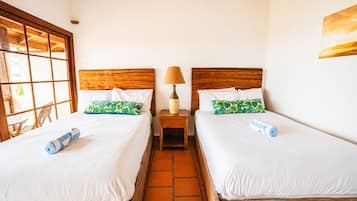 A hotel room with two beds, a nightstand with a lamp, and a window with a view.