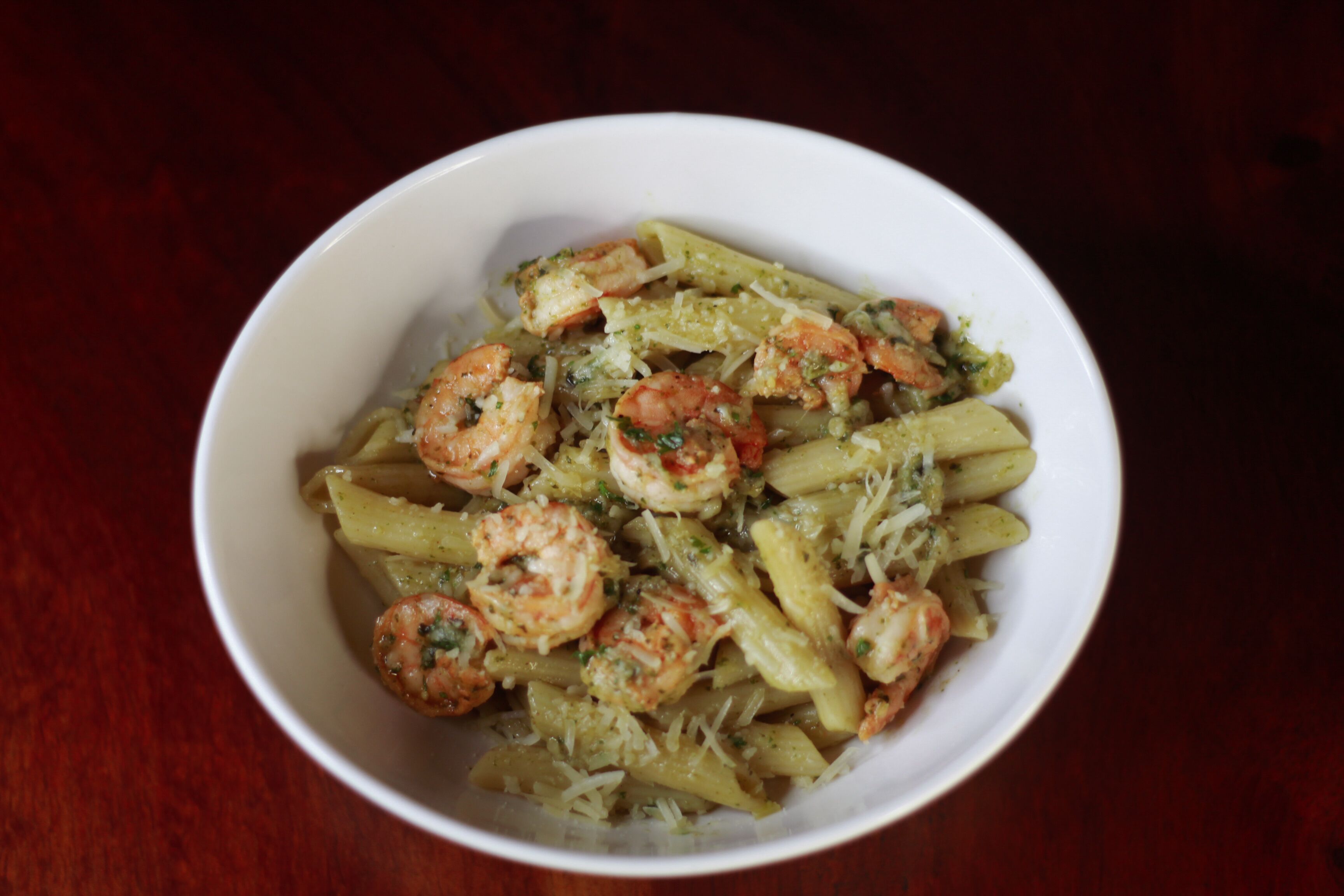 A bowl of pasta with shrimp and a green sauce.